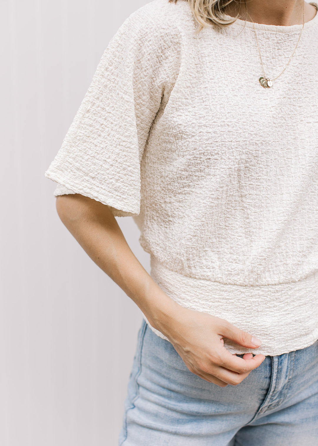 Close up of texturing on a cream short sleeve top with a round neck and elastic waistband.