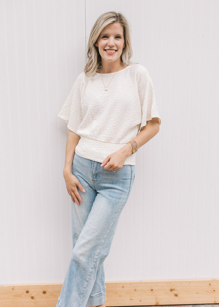 Model wearing jeans and a cream short sleeve top with round neck, elastic waist and slightly crop.