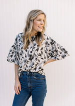 Model wearing jeans with a cream top with a black floral pattern and bubble short sleeves