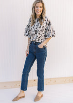 Model wearing jeans, mules and  a cream top with a black floral pattern and bubble short sleeves