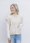 Model wearing a cream cable knit sweater with front pouch pockets and capped short sleeves.