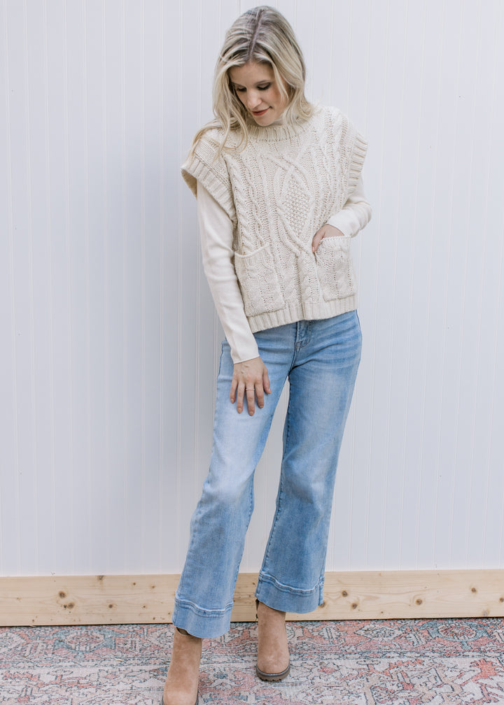 Model wearing jeans, booties and a cream cable knit sweater with capped short sleeves.