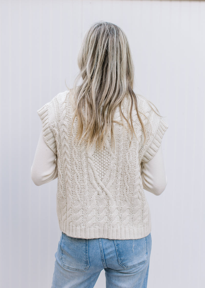 Back view of Model wearing a cream cable knit sweater with capped short sleeves.