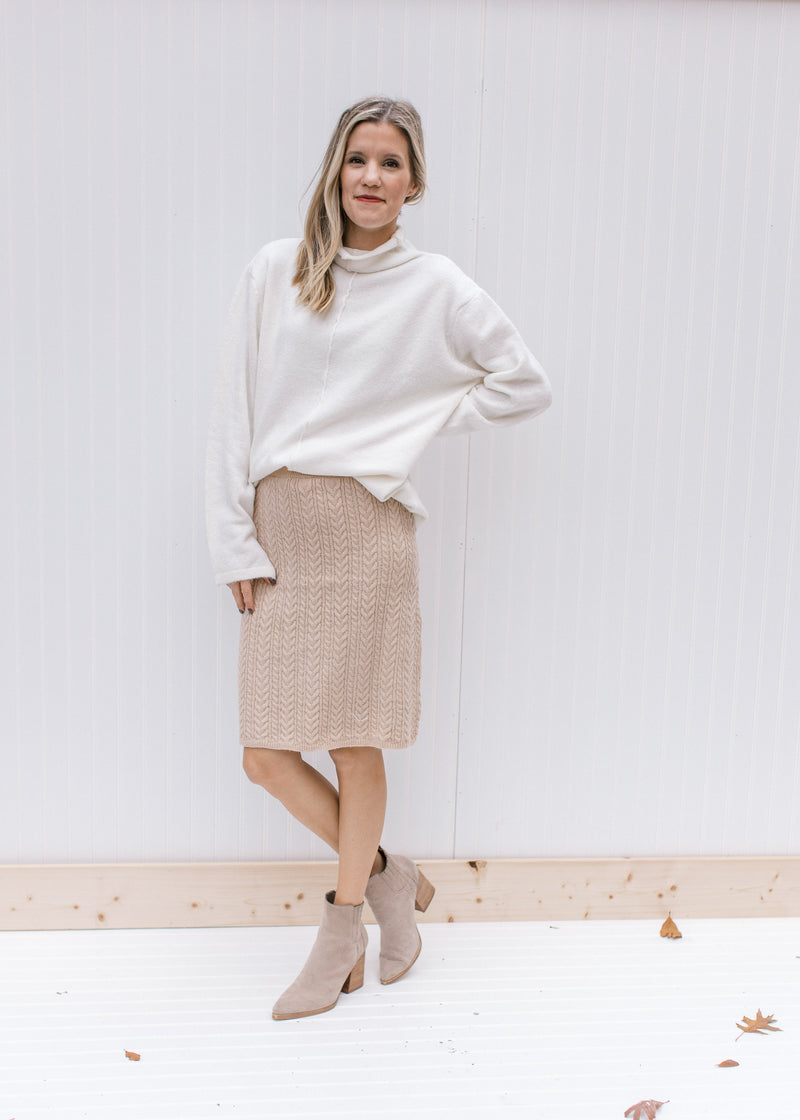 Model wearing booties and an off white sweater with a cream cable knit skirt, hitting above the knee