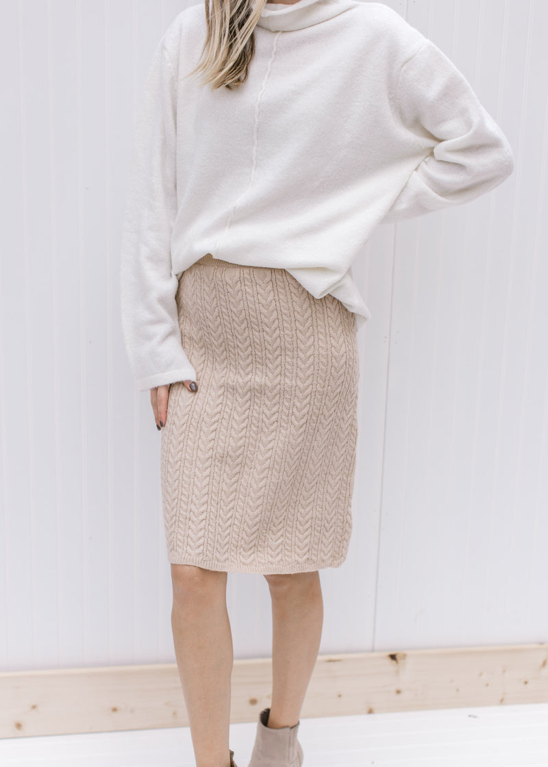 Model wearing a cream cable knit skirt, hitting just above the knee with an elastic waist band. 