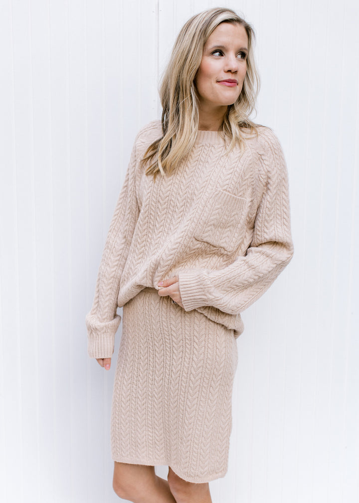 Model wearing a cream cable knit skirt, hitting just above the knee with a matching sweater. 