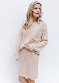 Model wearing a cream cable knit acrylic sweater with a matching cream skirt, hitting above the knee