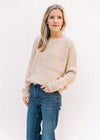 Model wearing a cream cable knit sweater with a patch pocket and long sleeves tucked into jeans.