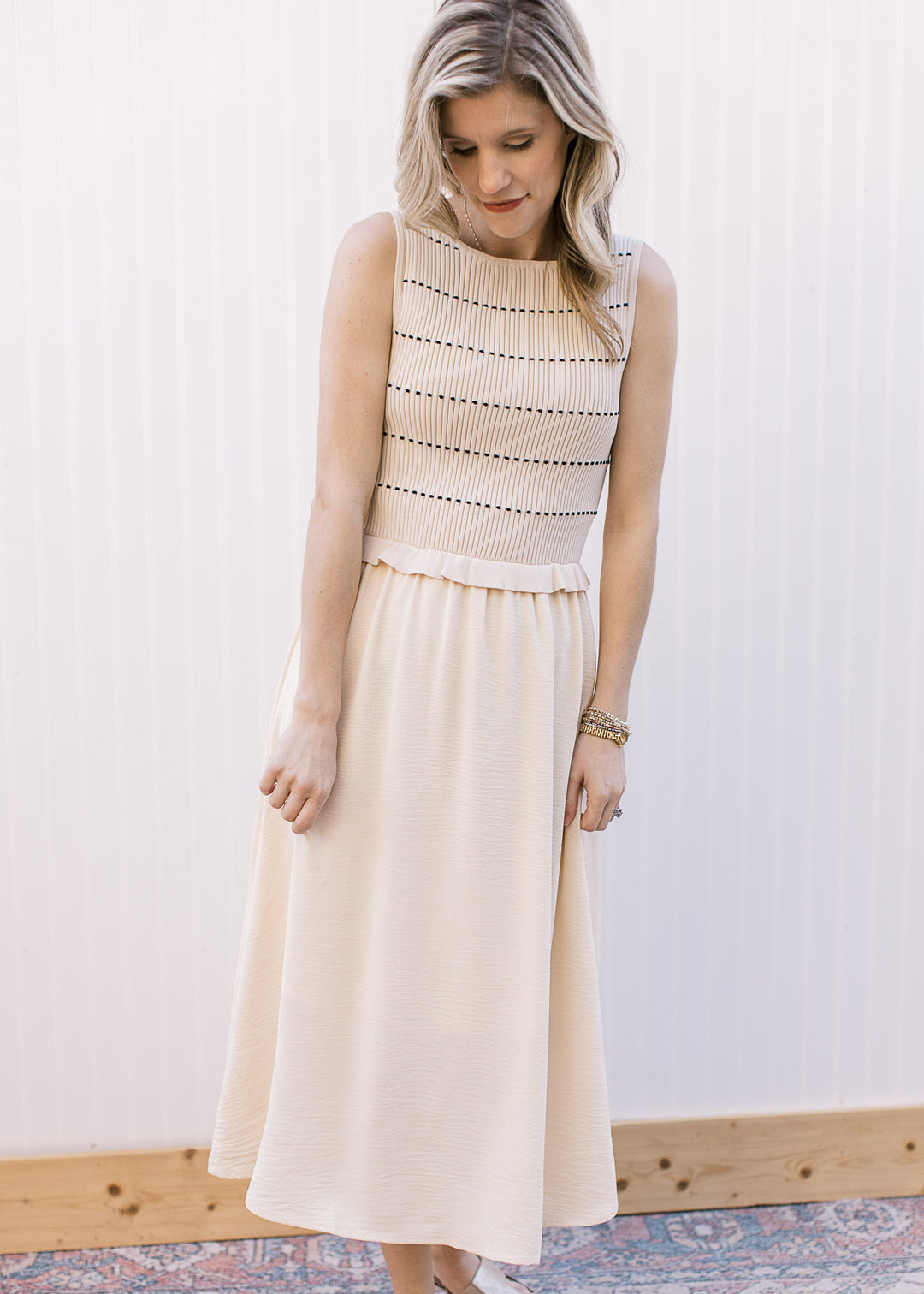 Model wearing a cream midi dress with attached sleeveless ribbed sweater with black stripes.