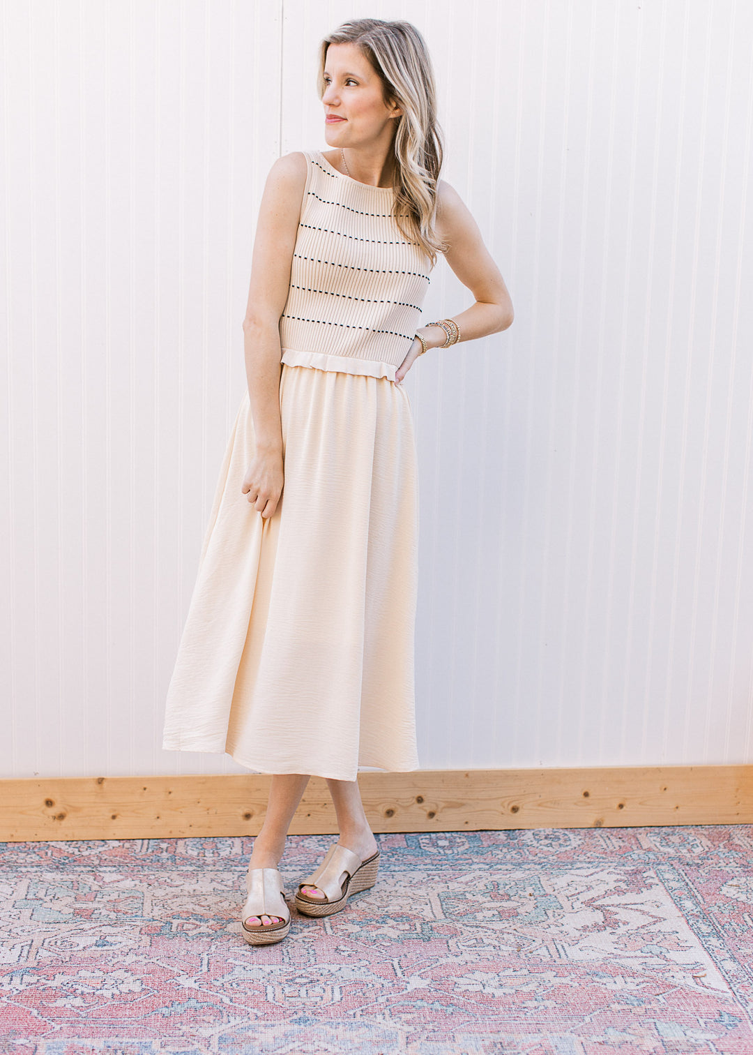 Model wearing sandals and a cream midi dress with a sleeveless ribbed sweater with black stripes.