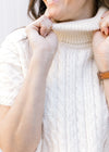Close up of cowl neck on a cream sweater with a cable knit fabric and short sleeves. 