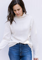 Model wearing a cozy cream turtleneck sweater with long sleeves and a split hem at the cuff.