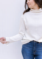 Close up of split hem at the cuff of a long sleeve cream sweater with a turtleneck.