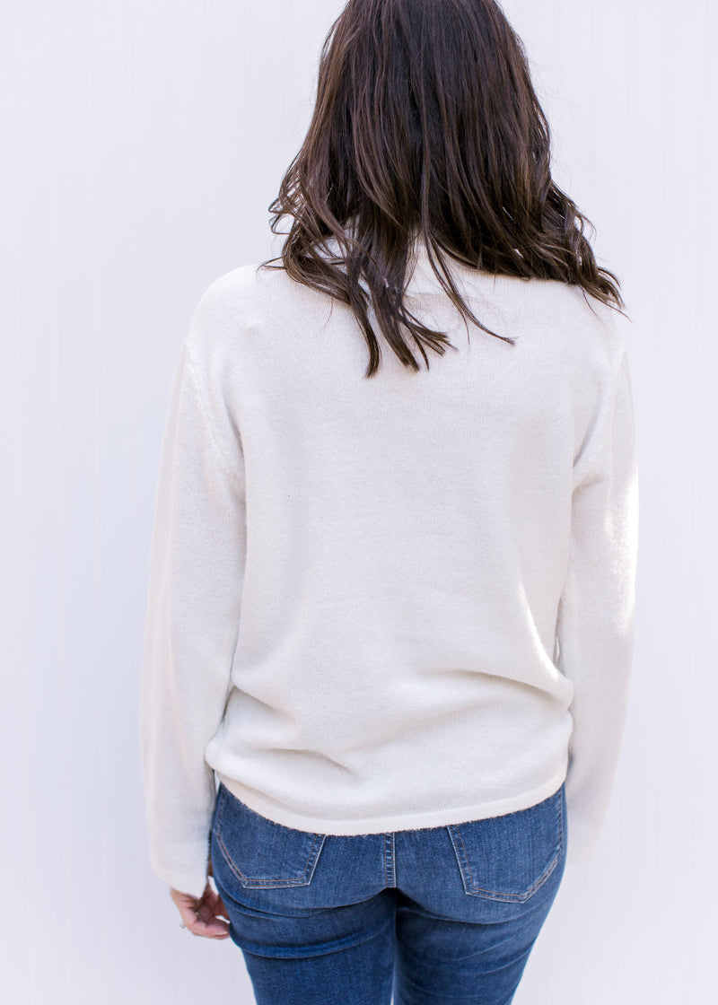 Back view of Model wearing a cream turtleneck sweater with long sleeves and a split hem at the cuff.