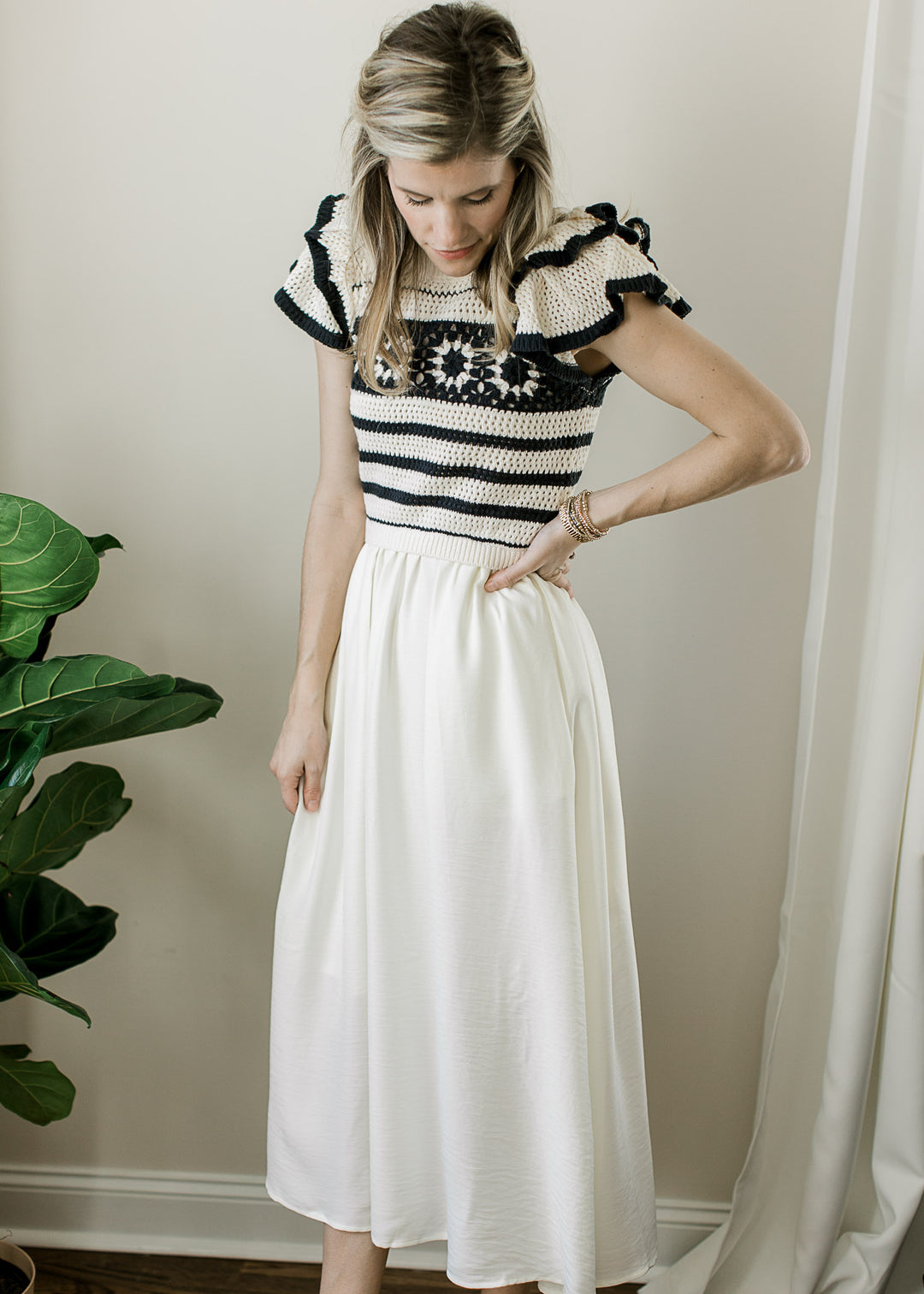 Model wearing a cream skirt with attached crochet sweater with black stripes and flutter sleeves.