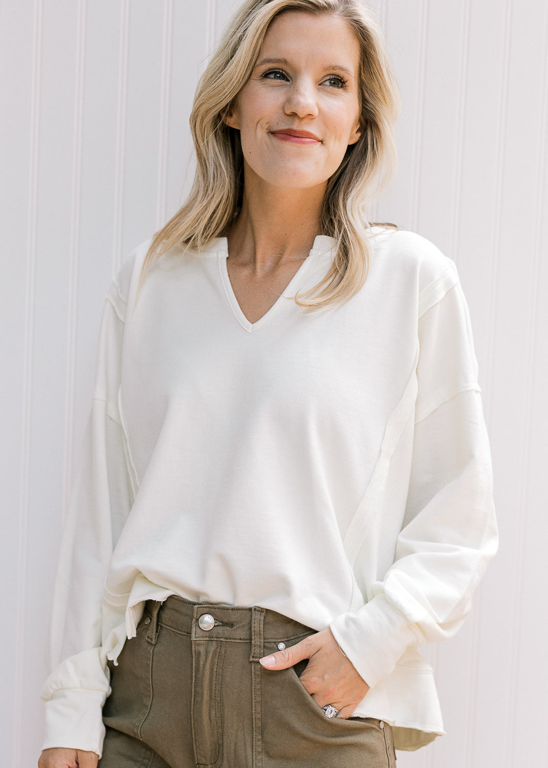 Model wearing a long sleeve cream lightweight sweatshirt with a v-neck and unfinished hem. 