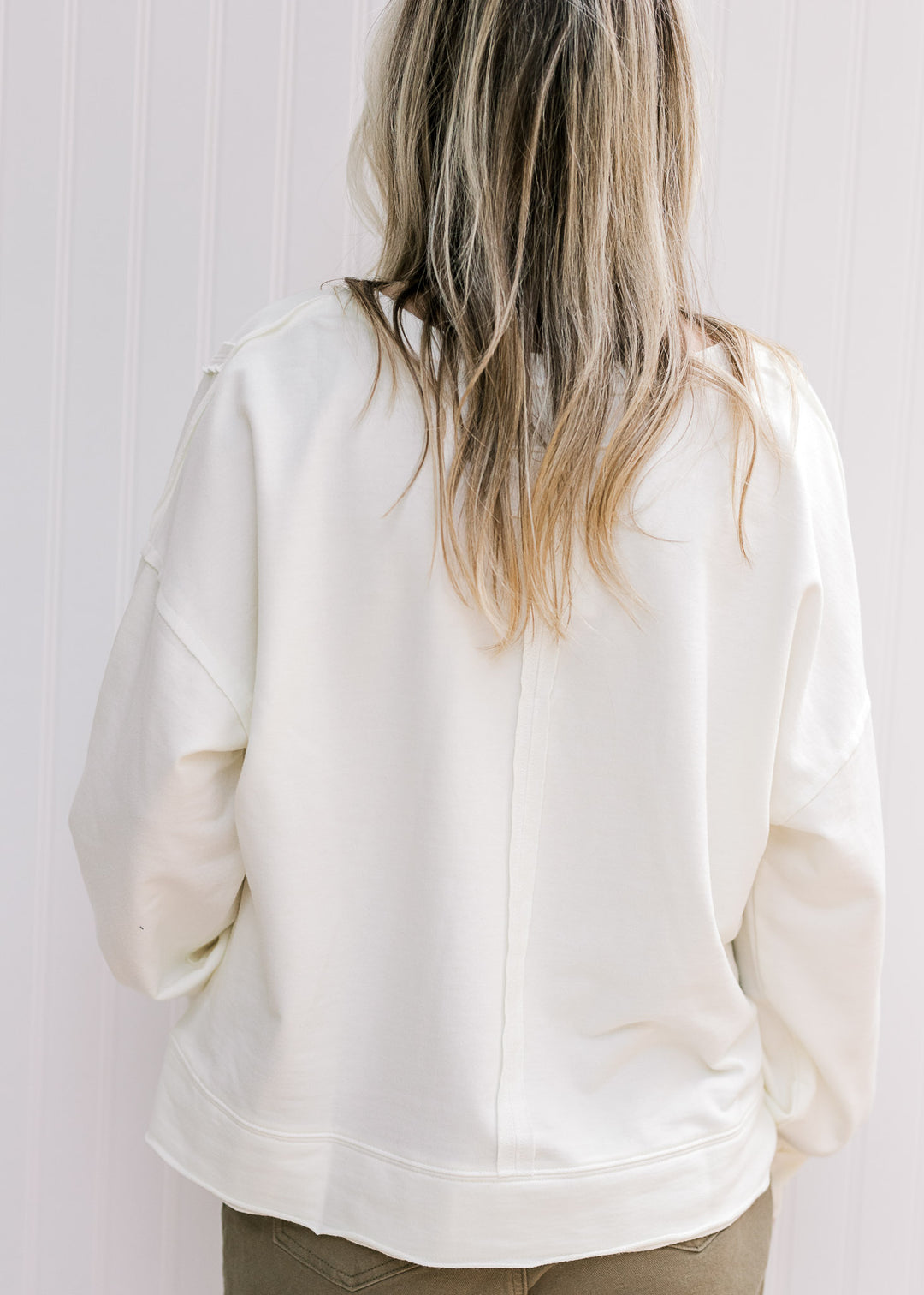 Back view of Model wearing a long sleeve cream lightweight sweatshirt with an unfinished hem. 