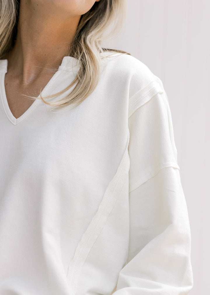 Close up of v-neck and unfinished hem on a cream lightweight sweatshirt with long sleeves. 