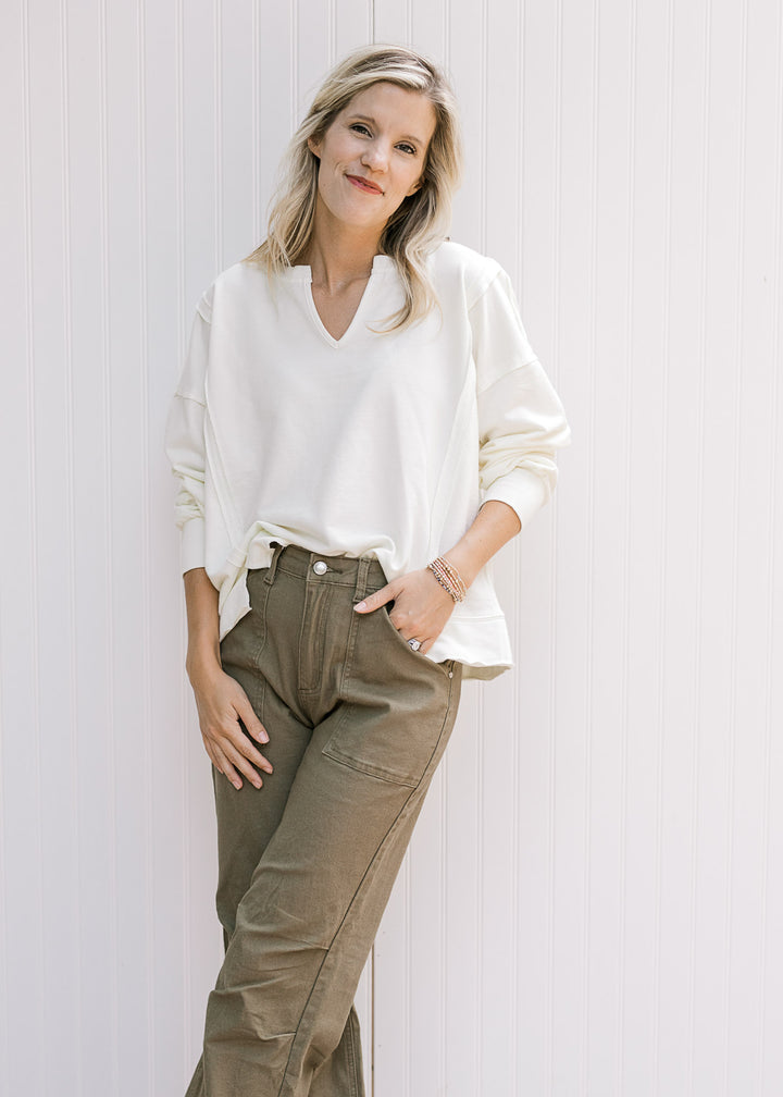 Model wearing green denim and a long sleeve cream sweatshirt with a v-neck and unfinished hem. 