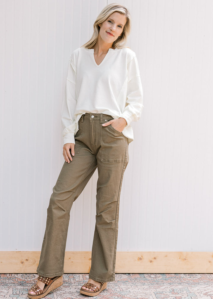Model wearing sandals, green jeans and a long sleeve cream top with a v-neck and unfinished hem. 