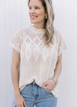 Model wearing a cream short sleeve top with an open diamond weave and capped sleeves.