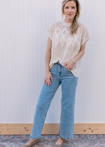 Model wearing jeans, flats and a cream short sleeve top with an open diamond weave. 