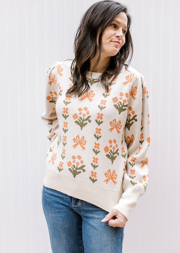 Model wearing a cream sweater with orange and green floral, round neck and long sleeves. 
