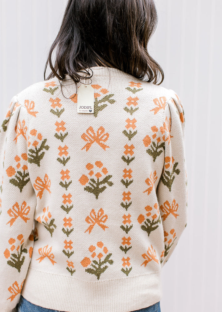 Back view of Model wearing a cream sweater with orange floral, round neck and long sleeves. 