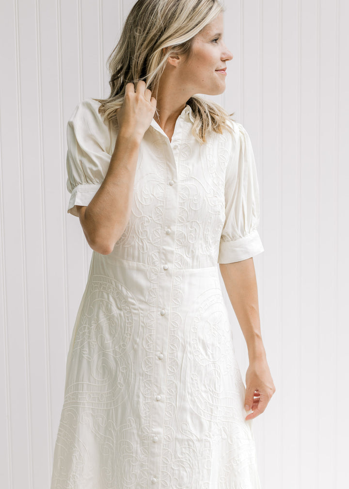 Model wearing a cream midi dress with a button closure, scalloped neck and short sleeves. 