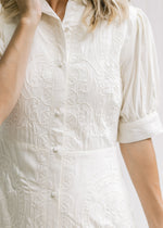 Close up view of embroidered detail and cuff on short sleeves of a cream midi dress. 