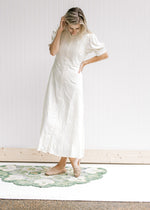 Model wearing flat mules with a cream dress with an embroidered detail and a button down front. 