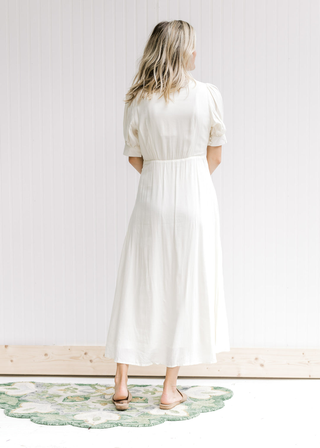Back view of Model wearing a cream embroidered dress with a button front and scalloped collar.