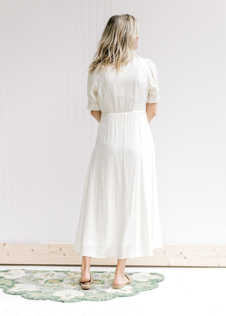 Back view of Model wearing a cream embroidered dress with a button front and scalloped collar.