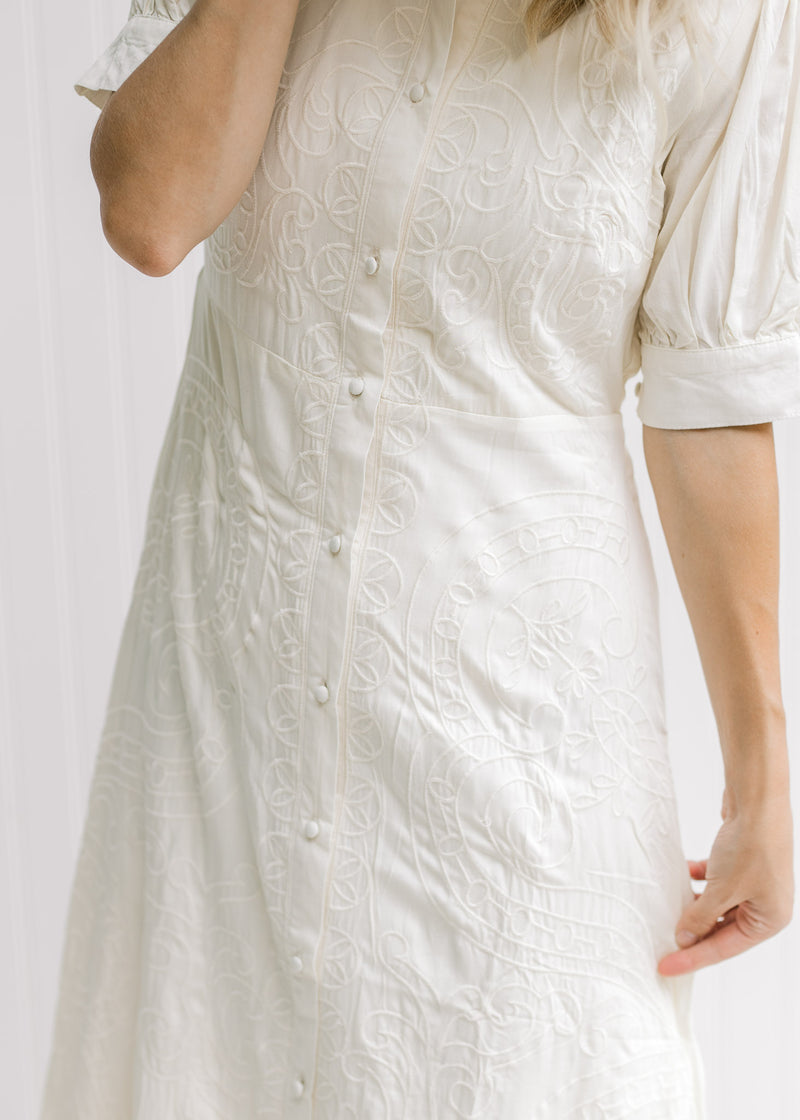 Close up view of button closure on a cream midi dress with an embroidered detail.