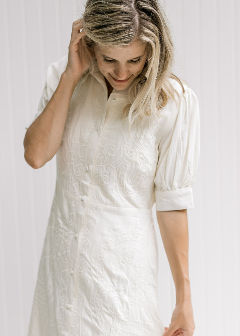 Model wearing a cream dress with an embroidered detail and short sleeves with a two button closure. 