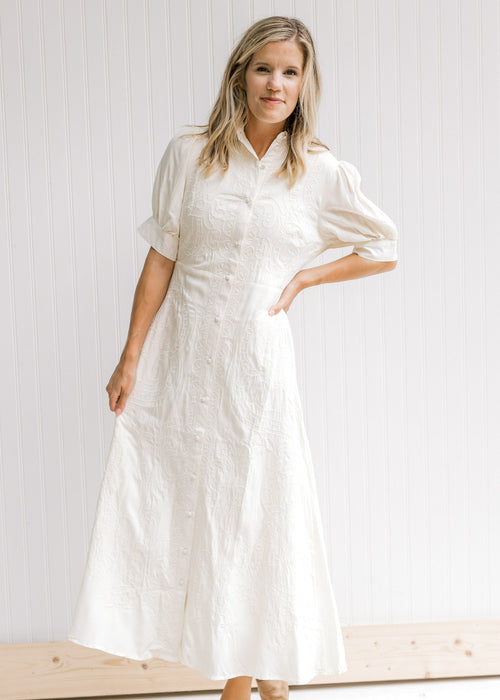 Model wearing a cream dress with an embroidered detail, button down front and scalloped collar. 