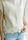 Close up of eyelet detail and scalloped hem on a cream short sleeve sweater. 