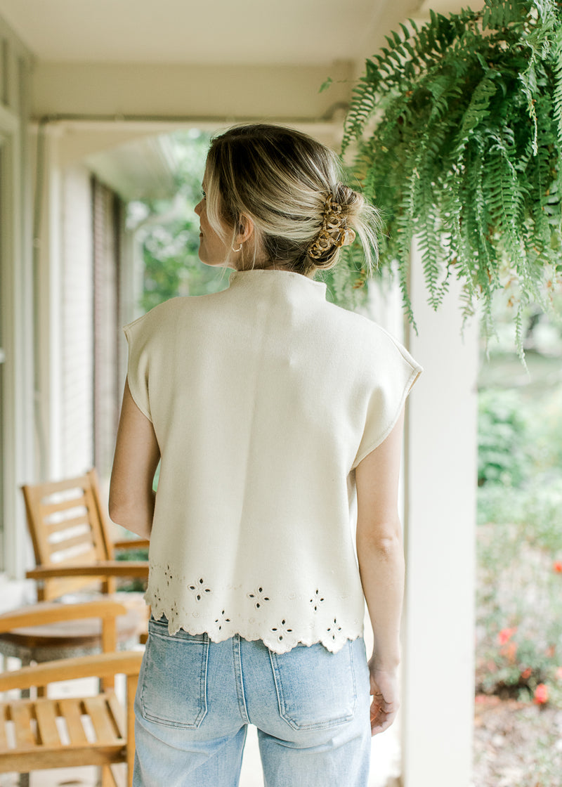 Back view of Model wearing a cream short sleeve sweater with a mock neck and eyelets at hem.