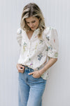 Model wearing a cream top with green and pink flowers, puff short sleeves and button front. 