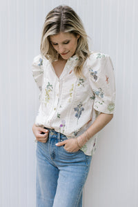 Model wearing a cream top with green and pink flowers, puff short sleeves and button front. 