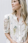 Close up of puff short sleeve with puff shoulder, button front on a cream top with flowers. 