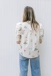 Back view of Model wearing a cream top with green and pink flowers and puff short sleeves.