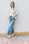 Model wearing jeans and a button up cream top with green and pink flowers and puff short sleeves.