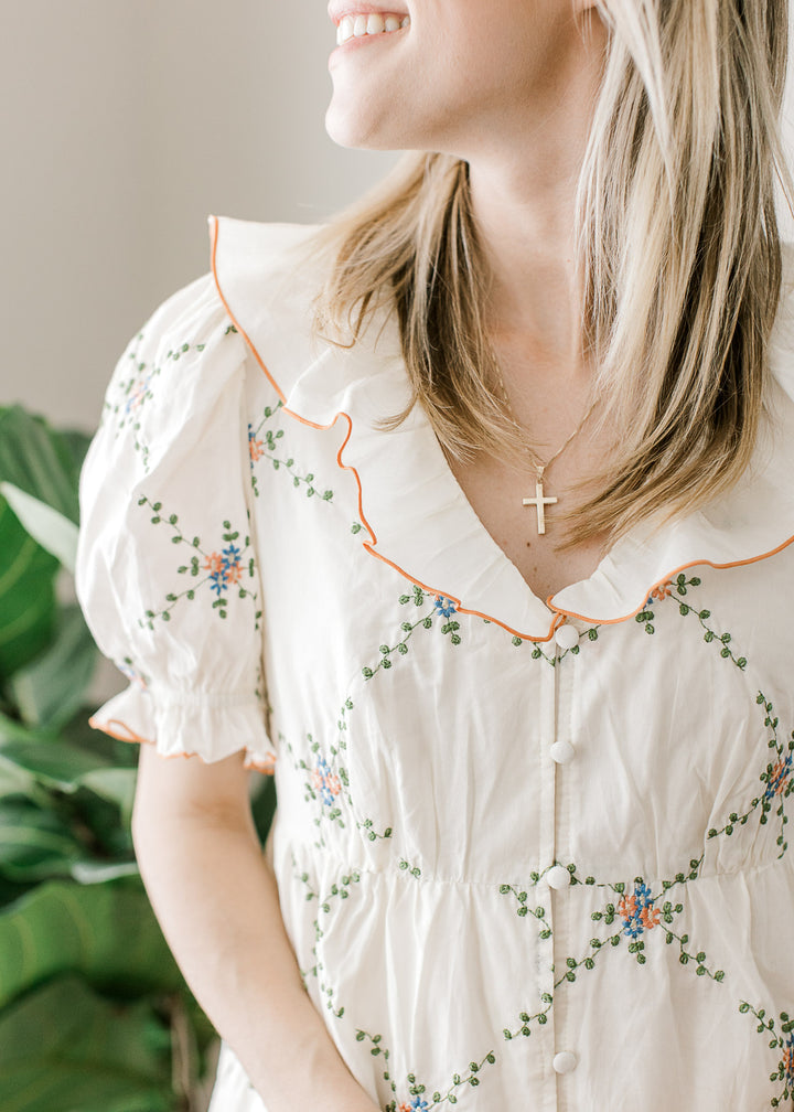 Close up of ruffle v-neck, bubble short sleeves and button front on a cream dress with floral. 