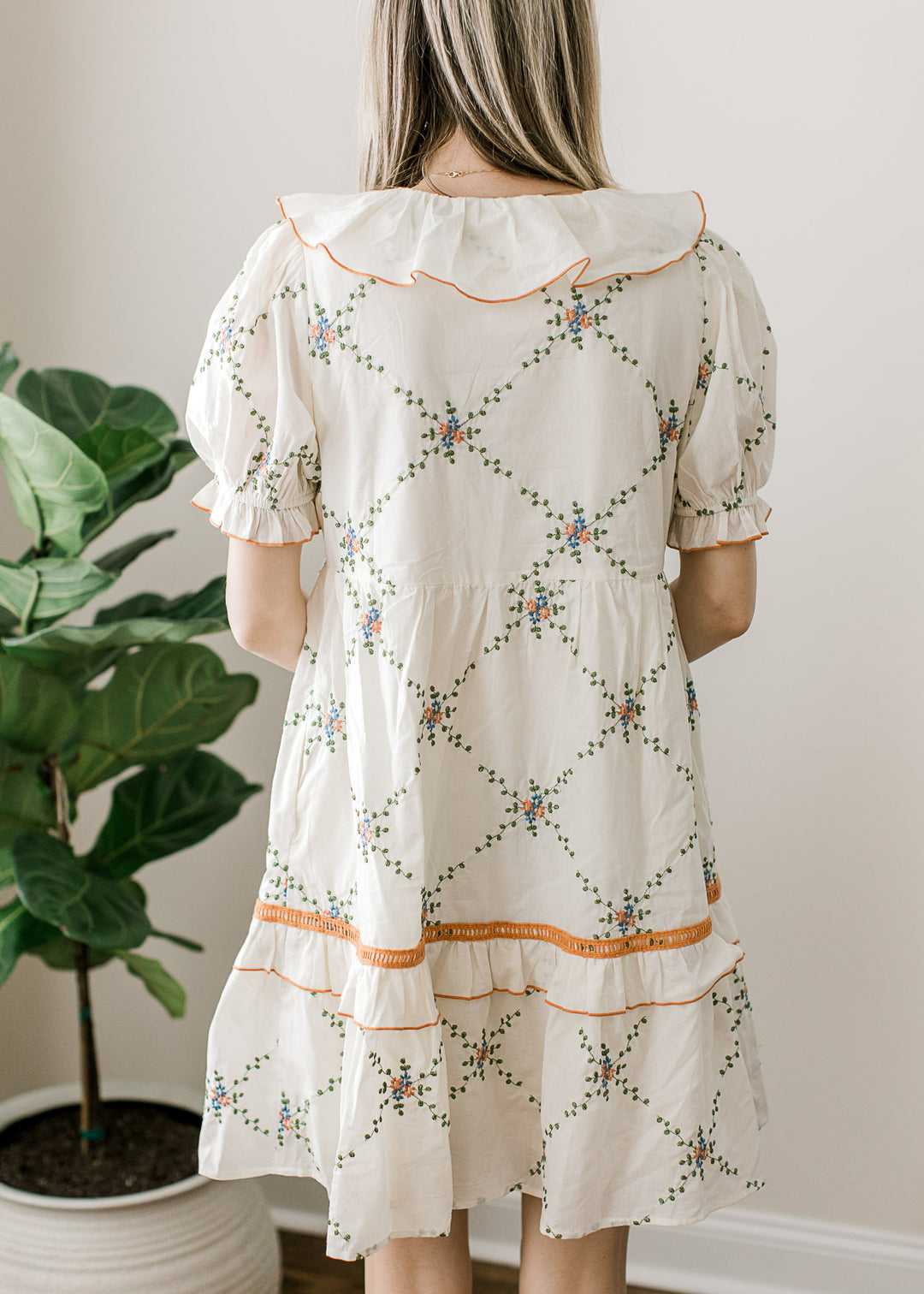 Back view of cream dress with embroidered lattice pattern and rust and blue floral accents.