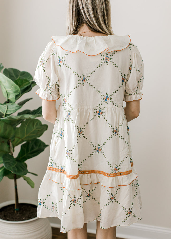 Back view of cream dress with embroidered lattice pattern and rust and blue floral accents.