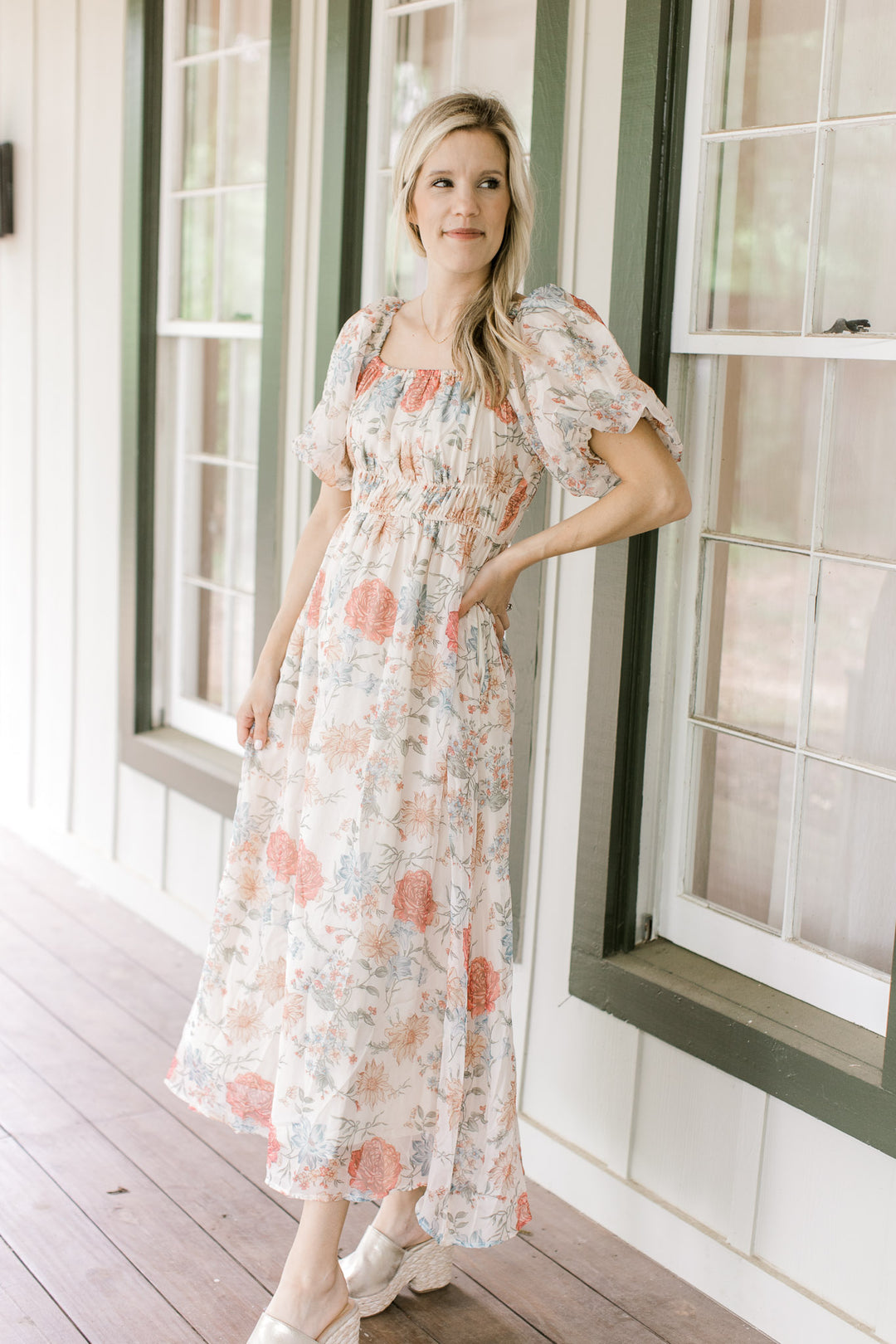 Model wearing a cream dress with pink, blue and yellow floral and bubble short sleeves.  