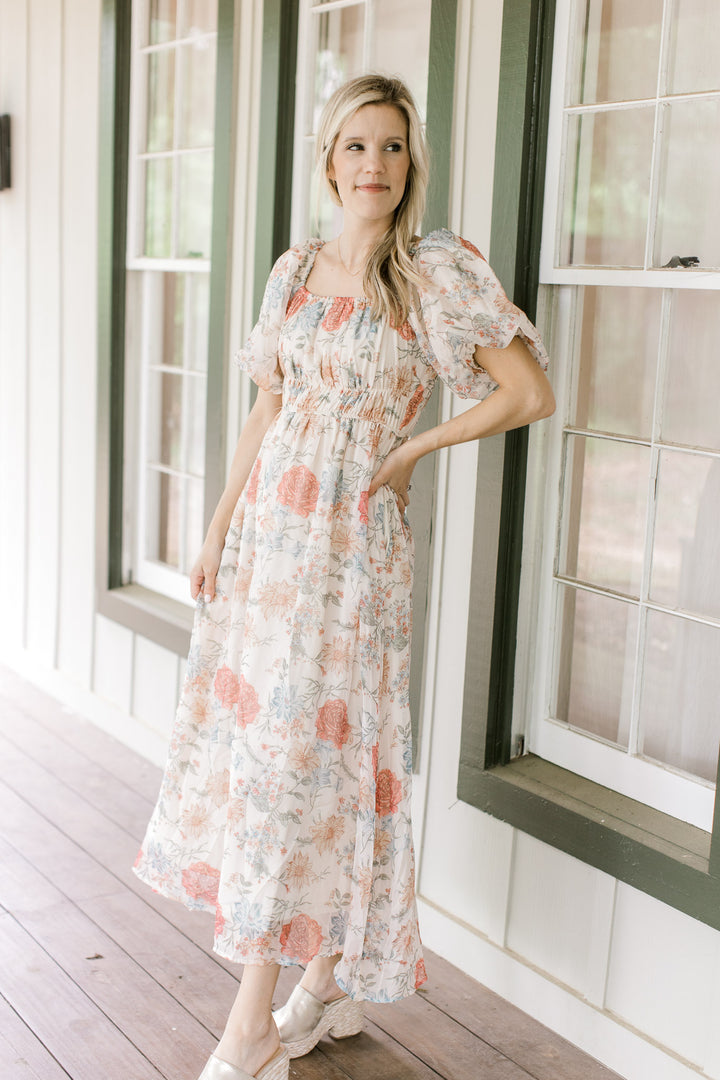 Model wearing a cream dress with pink, blue and yellow floral and bubble short sleeves.  