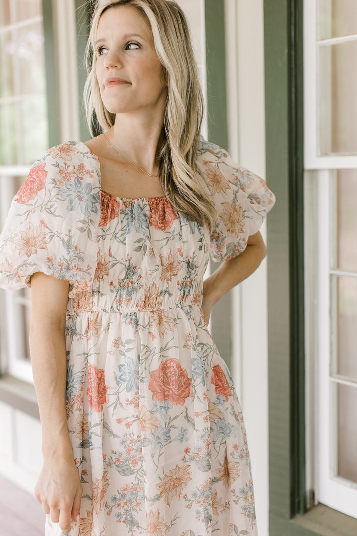 Close up of square neck and bubble short sleeves on a cream dress with floral pattern.