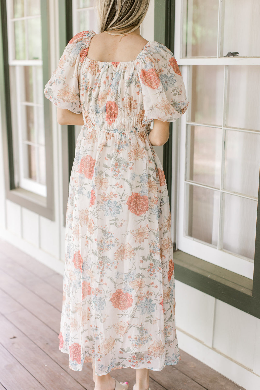 Back view of Model wearing a cream dress with pink, blue and yellow floral and bubble short sleeves.
